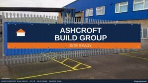 Navy and safety-orange Ashcroft Build Group mesh construction fence banner zip-tied to an industrial fence with brass grommets and mesh weave