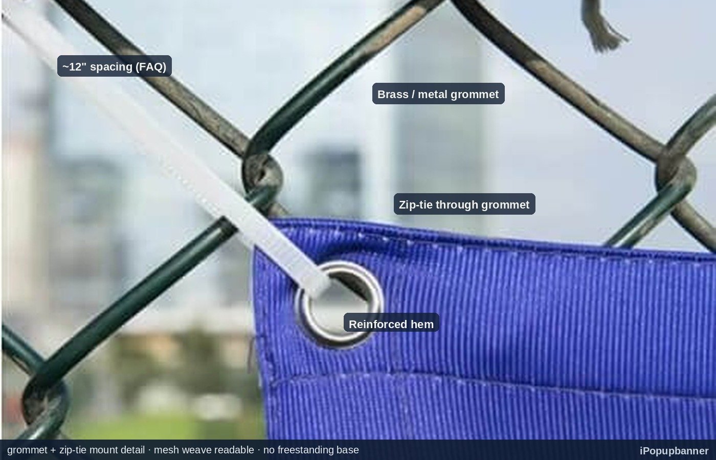 Close-up of brass grommets spaced along a reinforced hem on a mesh fence banner fastened to chain-link with black zip ties